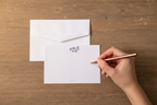 Hand writing on a card with an envelope on a wooden surface
