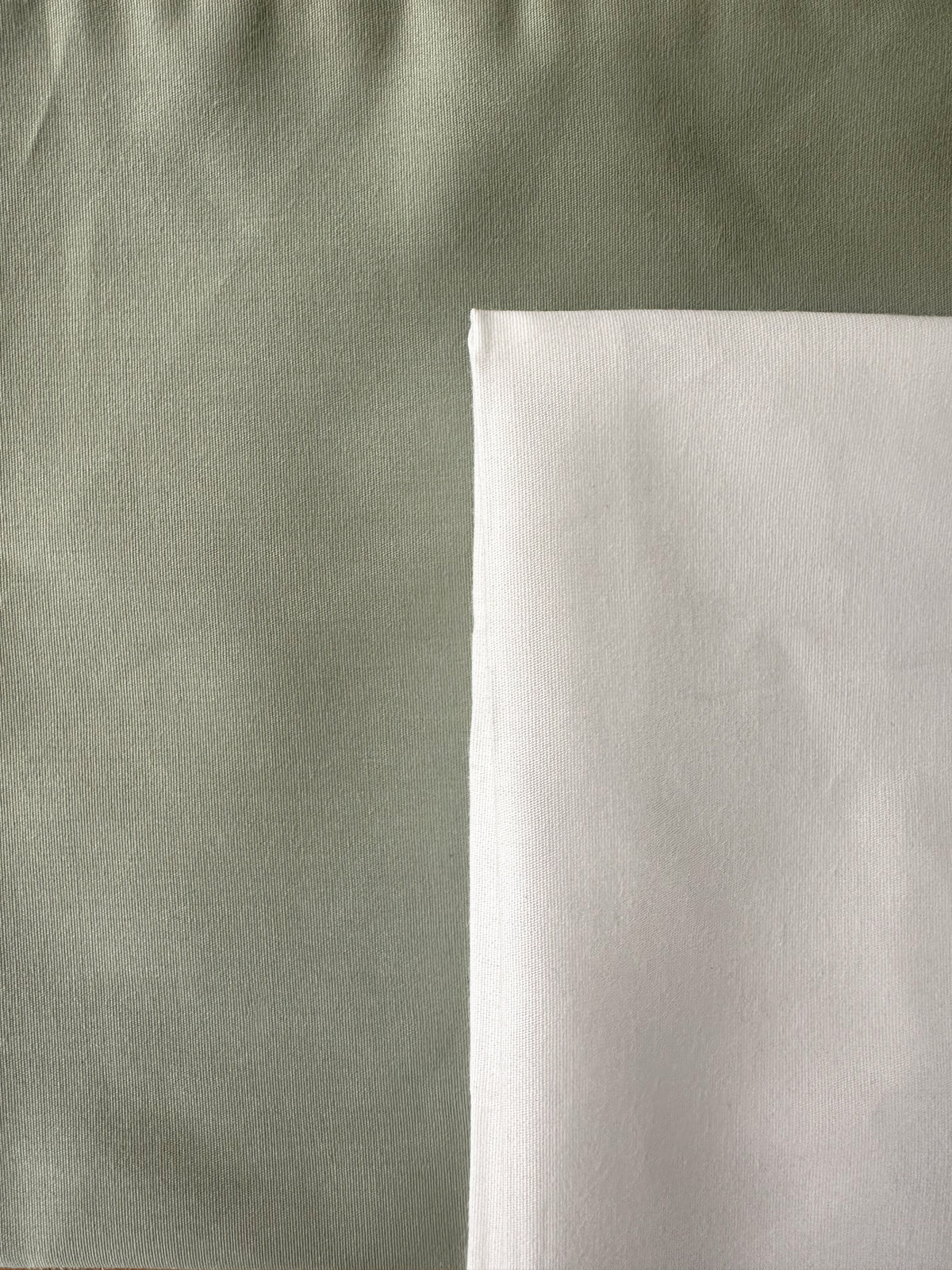 Two fabric swatches shown side by side, one in a muted sage green and one in a clean white, with the green swatch occupying the majority of the frame.
